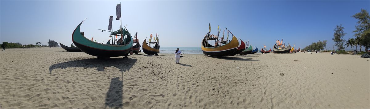 Colourful fishing boats resting across a wide sandy beach at Cox's Bazar